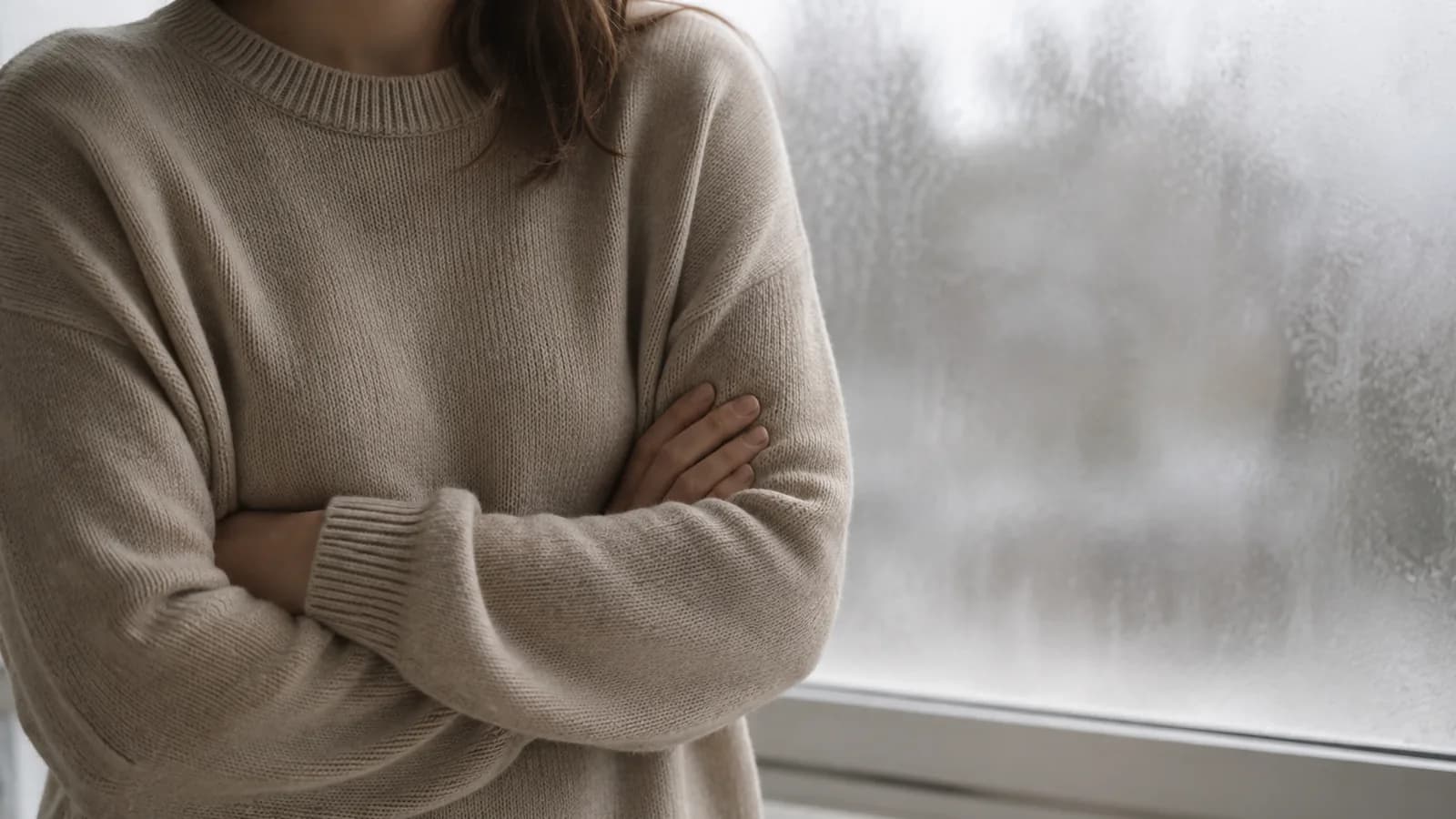 Folded arms in a knitted jumper with a frosted window behind.