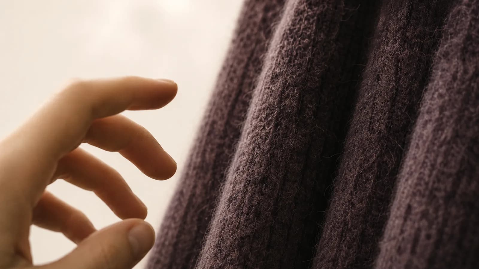 A close crop of coarse wool with a hand beginning to reach toward it.