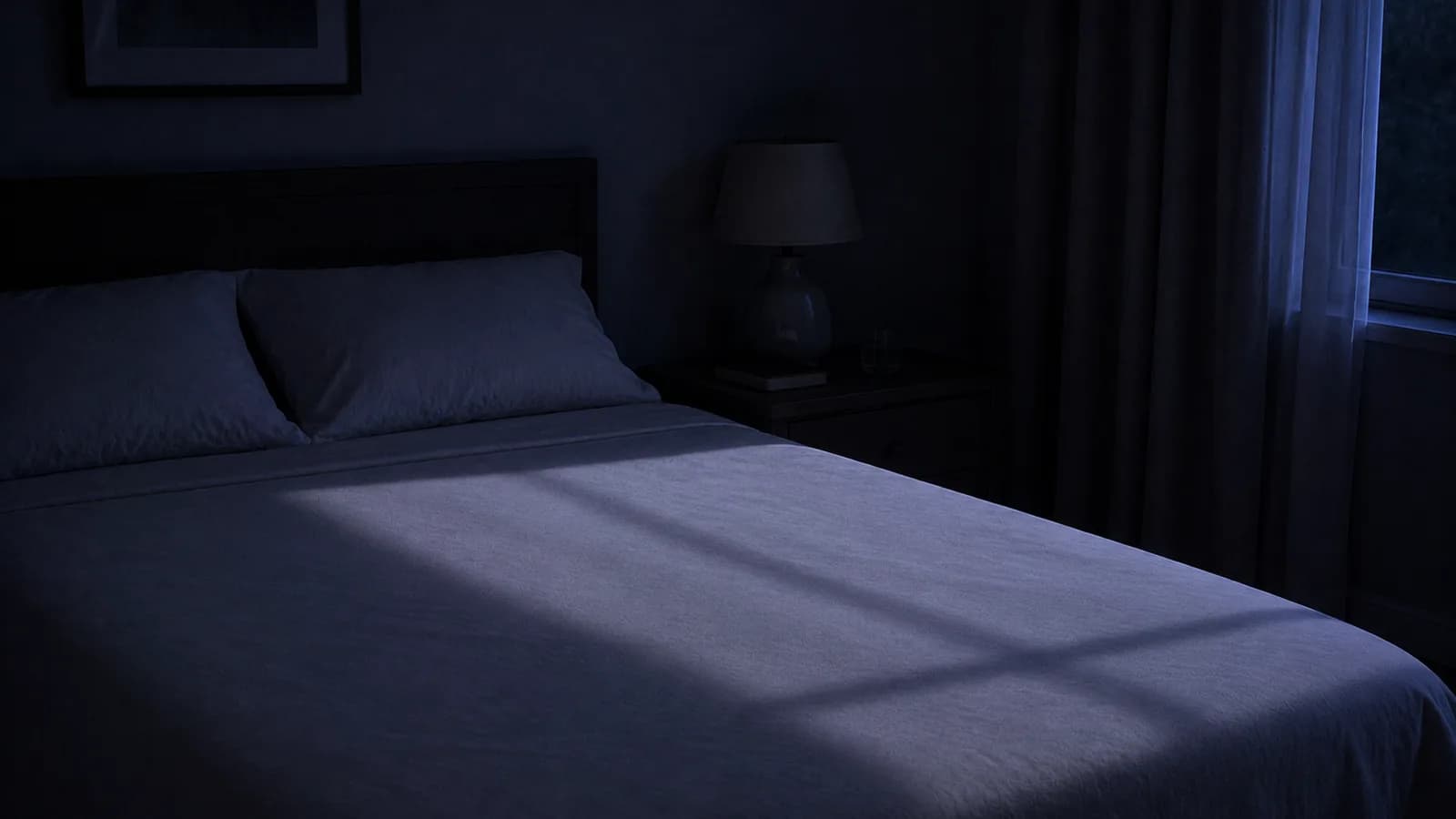 An empty bed at night with a long shadow lying across a flat duvet.