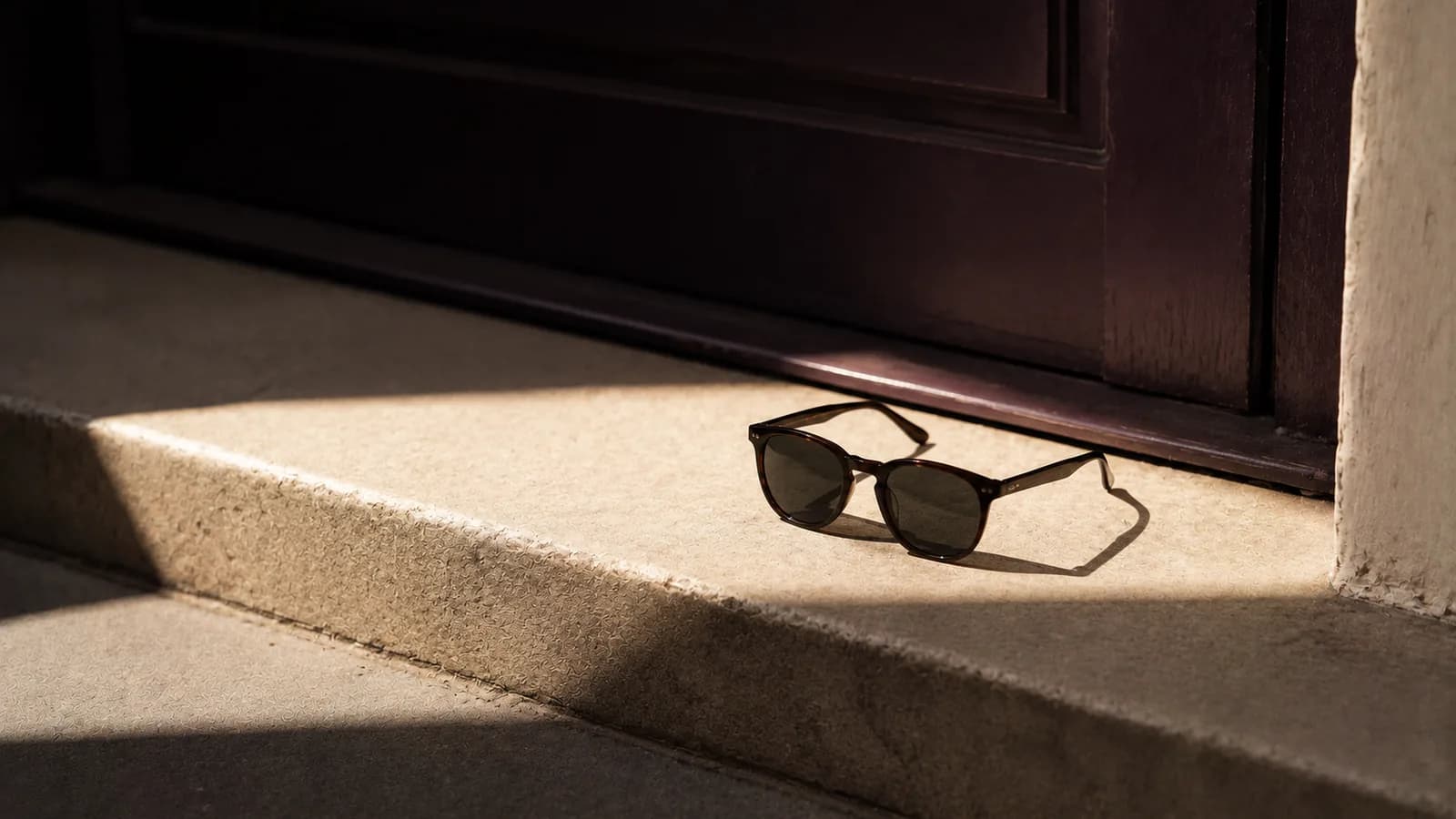 Sunglasses on a doorstep beside a shaft of bright sunlight.