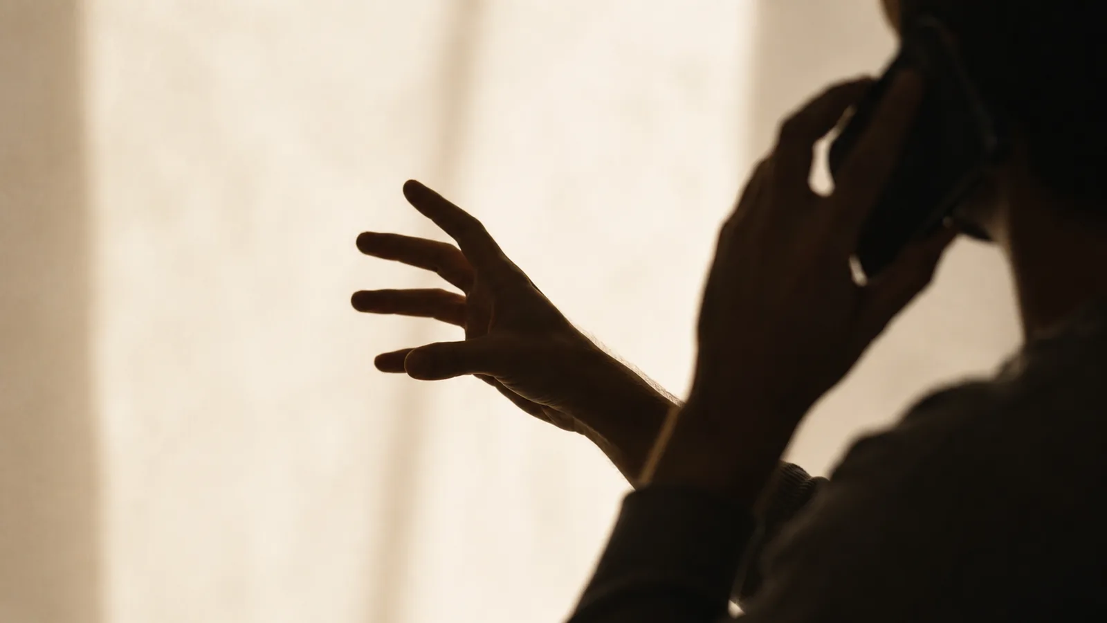 A hand caught mid-gesture beside a phone held to an ear.