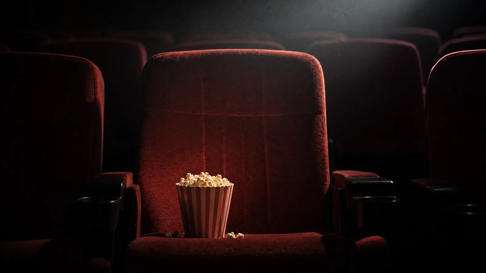 An empty cinema seat with popcorn, lit by off-screen projection light.
