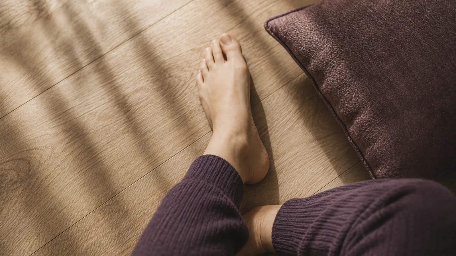 A bare foot on a wooden floor beside a cushion.