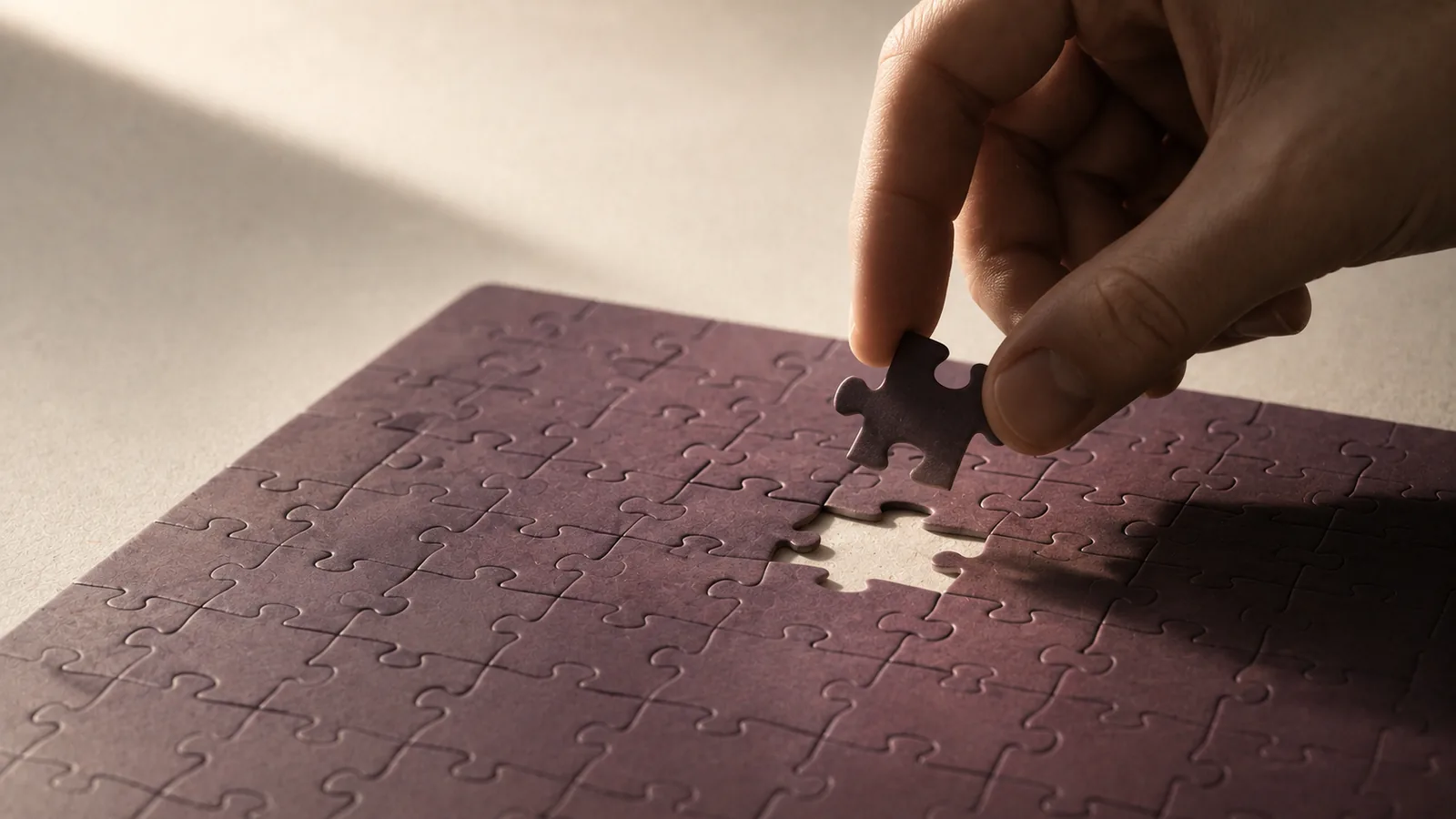 A nearly complete jigsaw with one piece held above the remaining gap.